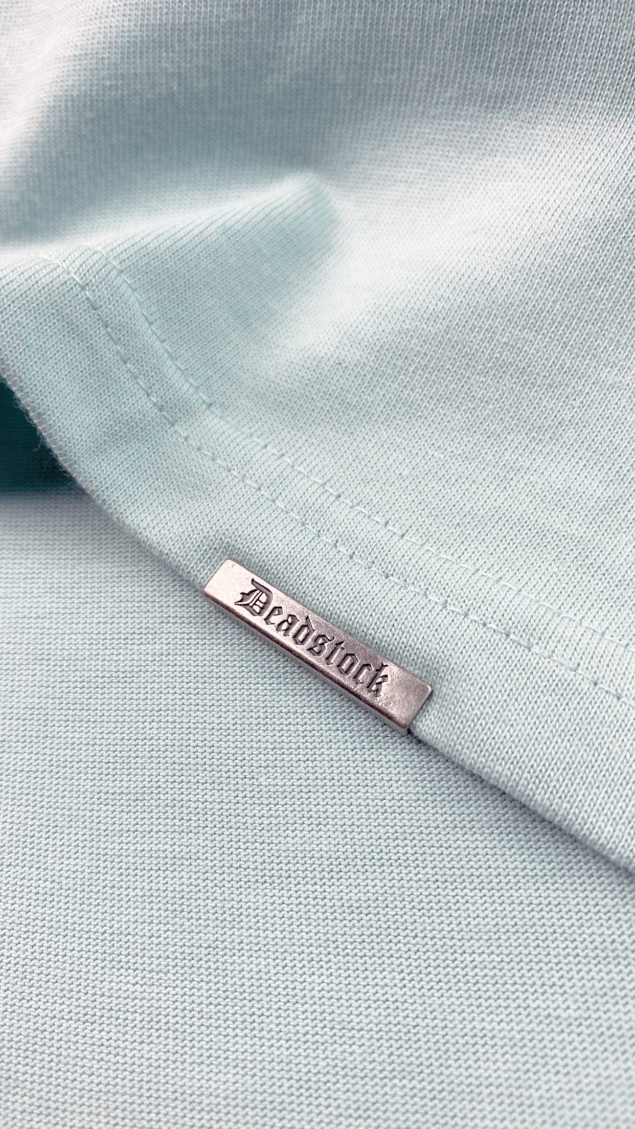 A blue t-shirt with a metal tag saying deadstock clamped to the rib of the shirt